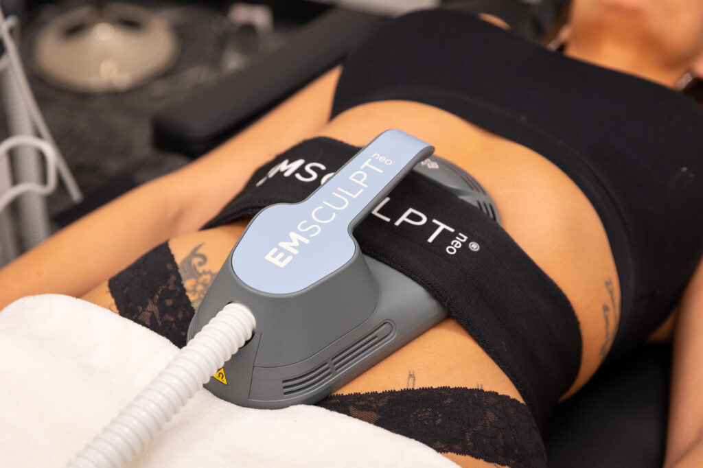 A patient lies down with a treatment applicator strapped to her abdomen for Emsculpt NEO near Prosper, TX.